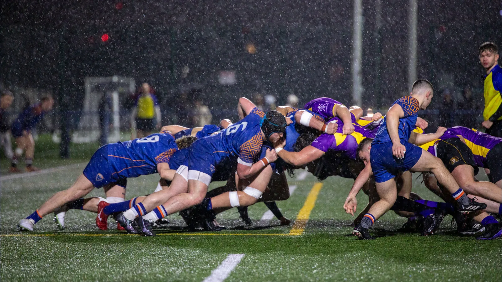 Mêlée de rugby de nuit sous la pluie et les projecteurs